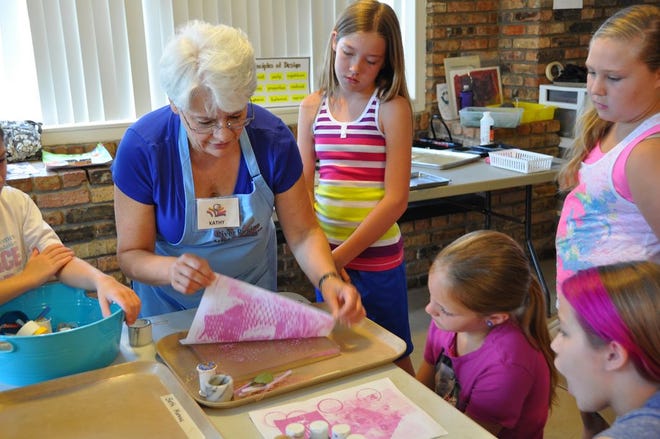 River Region Summer Art Camp students observe as Kathy Bourgeois pulls a mono print from a gelatin mold.