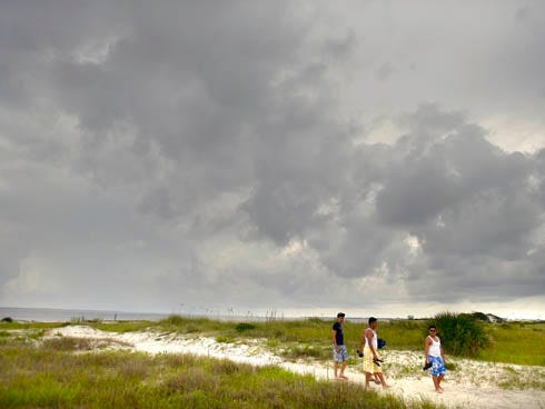 Beachgoers walk back to their car on Wednesday as rain clouds move over land from the Choctawhatchee Bay.