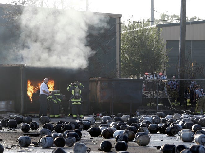 Firefighters keep an eye on a fire of plastic cylinder caps while standing in an area of exploded propane cylinders after an explosion and fire at a propane gas company Tuesday, July 30, 2013, in Tavares, Fla.