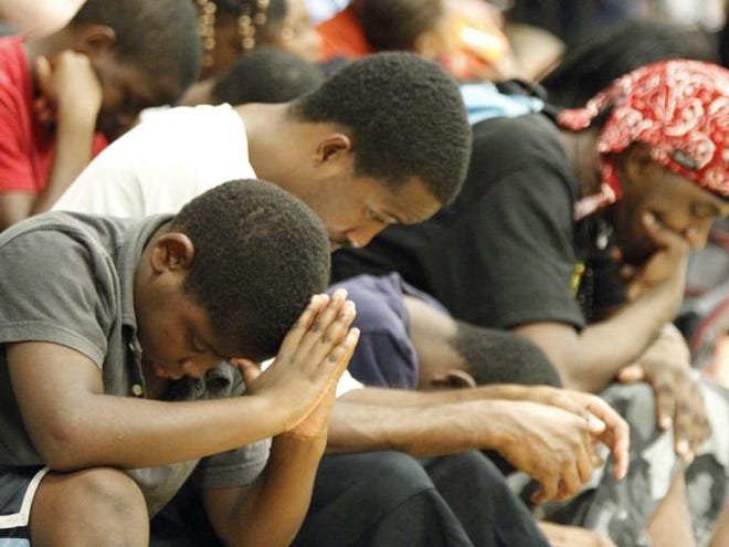 Nae'von Hatcher, 9, Cory McCray, 26, Jernard Dunbar, 10, and Joshua Lilly, 25, bow their heads Friday evening during an opening prayer by pastor Larry Johnson at the 13th Avenue Dream Center in east Bradenton just one day after hundreds of children and their parents witnessed two gunmen chase, shoot and kill a man at their youth football practice.