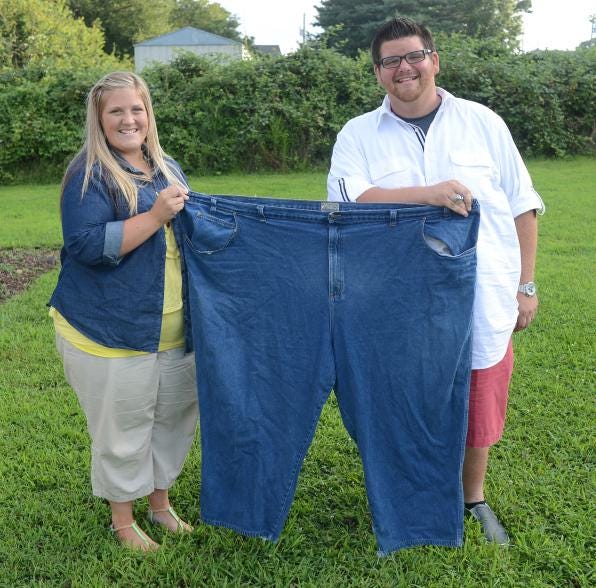 Summer and Jonathan Weaver hold up an old pair of jeans worn by Jonathan when he weighed over 200 pounds more than his current weight. Summer has lost more than 100 pounds in the same time frame.