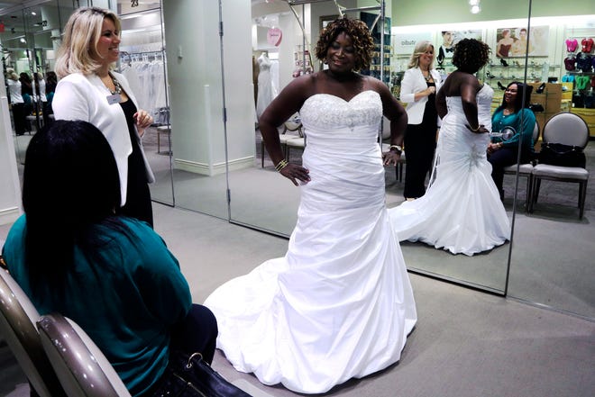 Sara Musillo, left, assistant store manager at David's Bridal in New York assists Yolanda Royal, 64, center as she tries on wedding dresses with her niece Angelic Lavine. Royal and her husband-to-be plan to spend about $11,000 on their wedding reception for about 100 people.