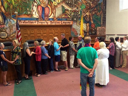 Nine same-sex couples take their wedding vows in the Santa Fe County Commission's chambers after receiving marriage licenses in Santa Fe, N.M., on Friday, Aug. 23. The Rev. Talitha Arnold, in white in foreground, of the United Church of Santa Fe officiated the ceremony. (AP Photo/Barry Massey)