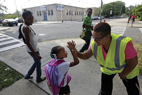 Safety Guard Renee Green high-fives Demari Hill, 5, as she heads to Gresham Elementary School with her parents Destiny and Anthony Hill on her first day of kindergarten classes on Monday, Aug. 26. 2013, in Chicago. Thousands of students will walk newly designated ?afe Passage?routes after CPS announced in May it would close about 50 schools and programs. Workers hired to help students get to and from school safely will be stationed along those routes, as well as police, firefighters and even public library security guards. AP Photos/M. Spencer Green