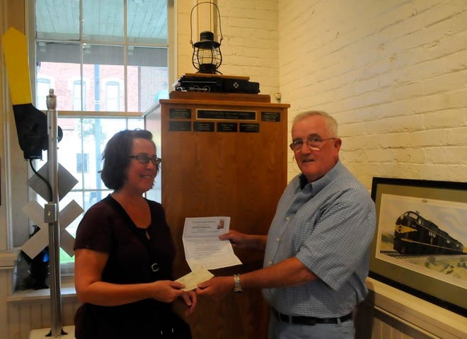 Eugene Baker, a member of the Hornell Erie Depot Museum's board of directors, presents Collette Cornish, museum director, with a check and a form Tuesday to have the name of his father-in-law, Fred H. Maas, placed on the museum's new railroad memorial, pictured here behind Baker and Cornish.
