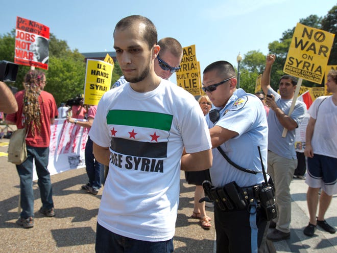A man in a "Free Syria" T-shirt, who is for military action in Syria, is arrested after spitting in the face of the man who said he was from Syria and against military action in Syria during a heated protest Saturday in front of the White House in Washington. The arrested man would not give his name.