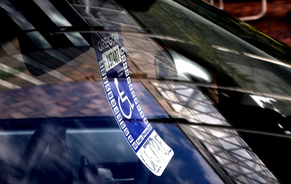 In this Sept. 3, 2013, photo, a handicapped parking tag hangs from the rearview mirror of a car parked at a metered parking spot in Portland, Ore.