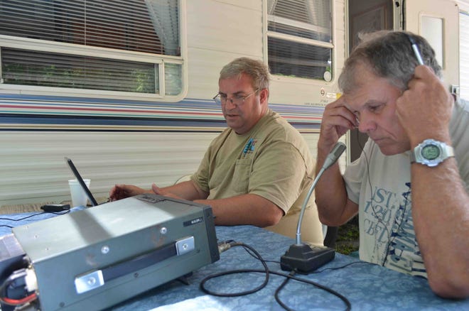 Retired Zeeland teacher Ed Heyboer, right, adjusts his headphones while listening for a response to his radio call. Jennison resident Kim Lobert, left, eyeballs equipment during the joint U.S.-Canada Field Day, which started Saturday. The men were broadcasting from Ottawa County Fairgrounds, where ham radio operators will work through 2 p.m. Sunday.