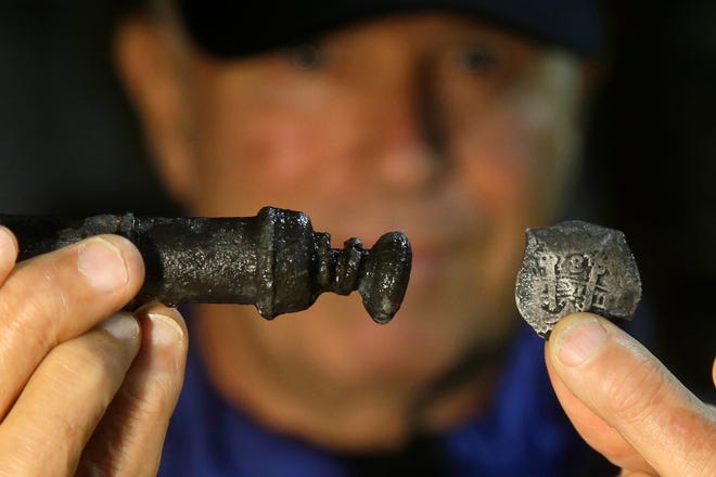 Underseas explorer Barry Clifford holds a piece of eight, right, and a metal syringe salvaged from the wreck of pirate ship "Whydah" during a video interview in Brewster, Mass., Tuesday, Sept. 17, 2013. Clifford discovered the wreck in 1984 in waters off Cape Cod Massachusetts.