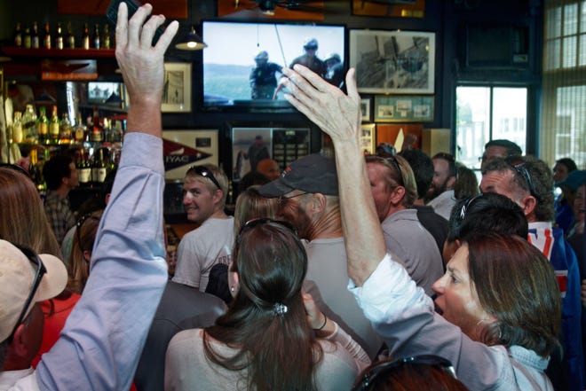Sailing fans salute Team Oracle’s win as they watch on TV at the International Yacht and Athletic Club on Thames Street in Newport.