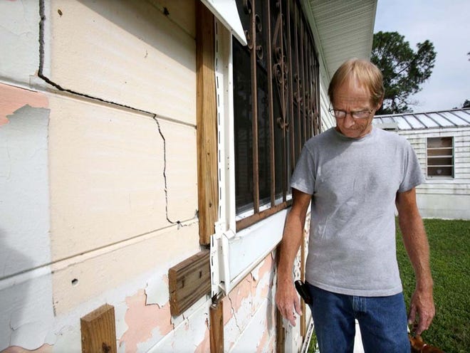 Gene Albritton looks at exterior cracks underneath the vinyl siding at his home in Winter Haven. Albritton's home is cracking all over the place and floors are tilting.