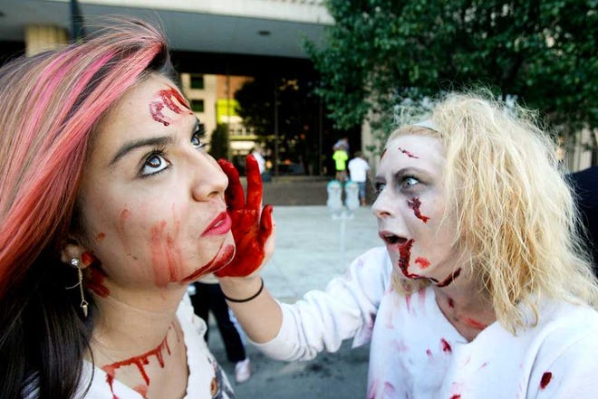 A zombified Molly Dillman, right, applies blood to Sabrina Serrano's face prior to Saturday night's Zombie Walk around the Statehouse.