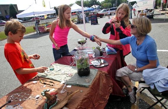 Brittany Randolph/Halifax Media Services From left, Eli Wolfe, 8, Akasha Wolfe, 11, Andie Winstead, 12, and Kathy McCurry chat over the Appalachian Mountain Terrariums and Beaded Jewelry booth set up at the Kings Mountain Farmers Market on Saturday.