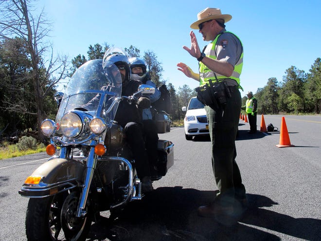 Grand Canyon National Park Ranger Jason Morris talks to people on a motorcycle at the closed park entrance on Thursday, Oct. 3, 2013 in Ariz.