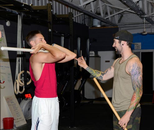 Sean Lazio, owner of BlackHorse CrossFit in Adrian, helps Taylor Hines of Adrian with the proper placement of his elbows while lifting.