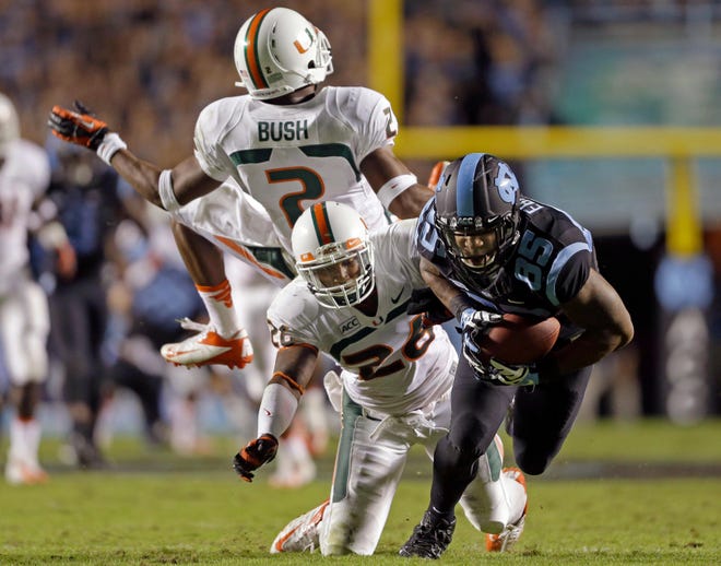 North Carolina’s Eric Ebron gains some yardage following a pass reception as Miami’s Deon Bush and Rayshawn Jenkins defend during Thursday night’s game in Chapel Hill. The Tar Heels wore black uniforms with blue trim against the 10th ranked Hurricanes as part of a ‘Zero Dark Thursday’ promotion.