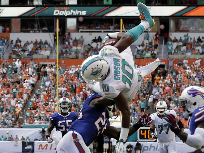 Miami's Brandon Gibson (10) jumps over Buffalo's Aaron Williams (23) and Da'Norris Searcy, obscured at right, for a touchdown during the first half Sunday in Miami Gardens.