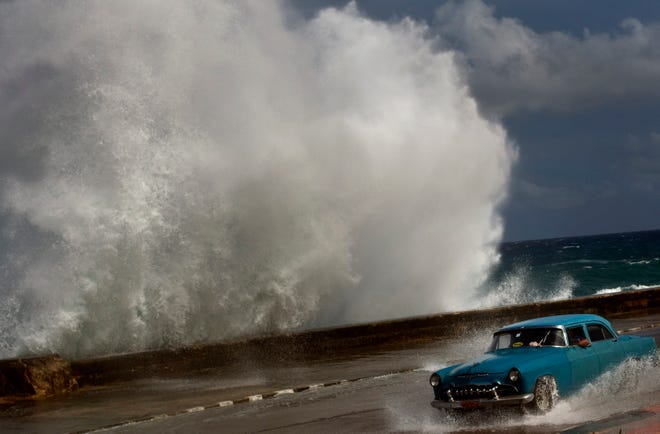 In this Thursday, Oct. 25, 2012 photo, a classic American car drives along a wet road as a wave crashes against the Malecon in Havana, Cuba. The following night, Sandy had passed the Bahamas and was being enveloped by an ordinary cold front coming off the Southeast. It was changing how it got its power, where its highest winds were and even what it looked like. But mostly it was getting bigger. And then it merged with a second storm, turned record huge and pivoted toward the U.S.'s largest city. (AP Photo/Ramon Espinosa)