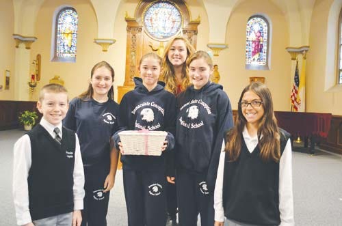 Immaculate Conception Student Council officers offer a gift basket containing more than $300 to Haley McCracken, background, who represents Project Self-Sufficiency in Newton.