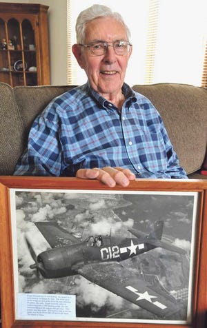 In this Oct. 10 photo, Roger Sorenson, 90, of Mattoon, sits at home holding a 1944 photo taken of himself flying a F6F Hellcat above Tinian Island in the Pacific Ocean as a Navy pilot during World War II.