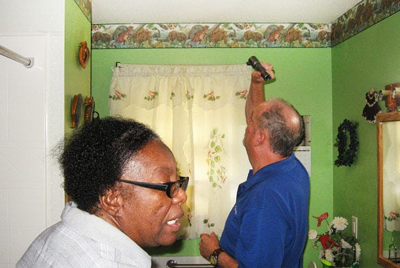 Brian McGinn, residential energy advisor for ElectriCities, shows Mildred Arrington a faulty bathroom venting fan that could be costing her more on her electric bill.
