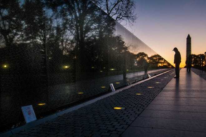 A visitor at the Vietnam War Memorial in Washington passes early in the morning on Veterans Day, Monday, Nov. 11, 2013, to look at the names inscribed on the wall. Several ceremonies are scheduled in the Nation’s Capitol to honor those who have served in the U.S. military including a wreath laying at Vietnam War Memorial. The Washington Monument is at right.