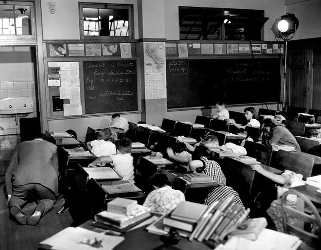 FILE - In this file picture, sixth grade students crouch under or beside their desks along with their teacher, Vincent M. Bohan, left, as they act out a scene from the Federal Civil Defense administration film "Duck and Cover" at Public School 152 in the Queens borough of New York City.