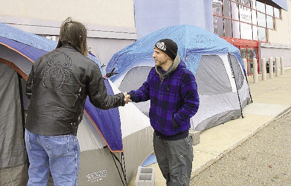 Tony Avitar of Akron, left, shakes the hand of fellow camper and bargain hunter Jonas Allooh of Willowick as both of the men stand outside of their tents in front of Best Buy in Cuyahoga Falls, Ohio. They hope to be the first in the door for holiday sales and get great deals on televisions and laptops.