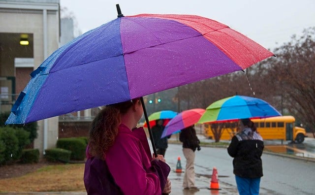 Emily Prychodko, a first year 3rd grade at Donna Lee Loflin, along with other teachers stand in the rain to offer students awaiting their ride a bit of shelter and a splash of color 11.26.13.(PAUL CHURCH / THE COURIER-TRIBUNE)