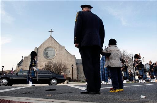 A police officer holds his son's hand outside a church during the funeral for Michael Feeney Tuesday, Dec. 3, 2013, in Ridgewood, N.J. Feeney, 10, was named Ridgewood's honorary police chief for 2013 before succumbing to cancer last week. He had been struggling for four years with Ewing's sarcoma, a rare, aggressive and often fatal bone cancer that usually develops in children and young adults. (AP Photo/Mel Evans)