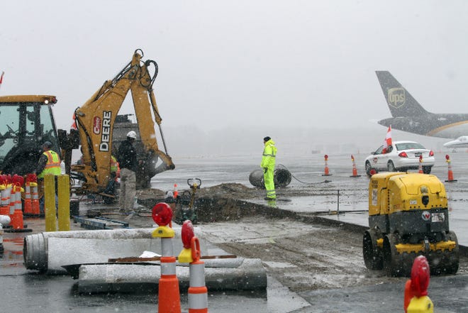 Workers toil through the snowfall at T.F. Green Airport Tuesday to install pipes — part of a system to capture deicing fluids.