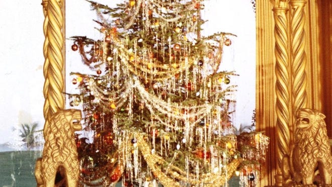 A vintage photo shows Marjorie Merriweather Post s festooned Christmas tree drenched in gold in front of the living room’s oceanfront windows at Mar-a-Lago. Photocredit: ©Hillwood Estate, Museum & Gardens