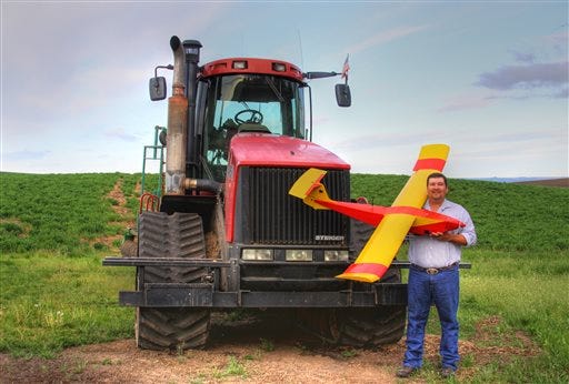 In this May 2013 photo provided by Rhonda Blair, farmer Robert Blair stands in front of his tractor holding an unmanned aircraft that he built in Kendrick, Idaho. Blair uses the home-made drone equipped with up to four cameras to "scout" his 1,500 acres of wheat, peas, barley and alfalfa and cow pasture. (AP Photo/Courtesy of Rhonda Blair)