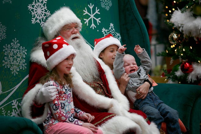 Sisters Rachel, 6. and Sophia Greenwood, 9, of Weymouth, smile for a photo with Santa as their 15-month-old brother, Dominic struggles to escape.