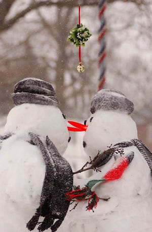A snowman and snowwoman are arranged so they appear to be preparing to kiss under mistletoe.