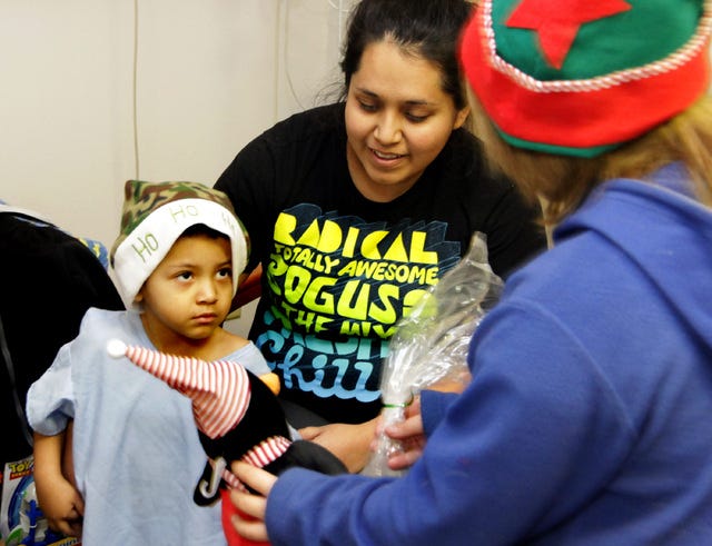 Jamie Mitchell Times Record - Dillion Landaverdo, 3, stays close to his mother, Jaqueline, Wednesday, December 25, 2013, as Fairview Elementery student Jennifer Bates presents a Christmas present to him during the school's eigth annual "Christmas in a Bag," toy give-a-way at Sparks Hospital. Fairview Elementery students assembled more than 600 Christmas hospital cheer bags with fruits and sweet treats and goodies to be given to patients in area hospitals.