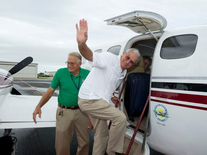In this photo provided by the Florida Keys News Bureau, Key West Mayor Craig Cates, right, waves goodbye as he boards a chartered aircraft at Key West International Airport Monday, Dec. 30, 2013, that flew to Havana, Cuba.