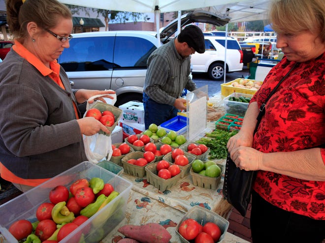 Gloria Castenholz, right, purchases tomatoes from Rusty and Mary Ludlam's produce booth at Dogwood Lane Farm at the Union Street Farmer's Market in downtown Gainesville, Fla., Wednesday, November 7, 2012.
