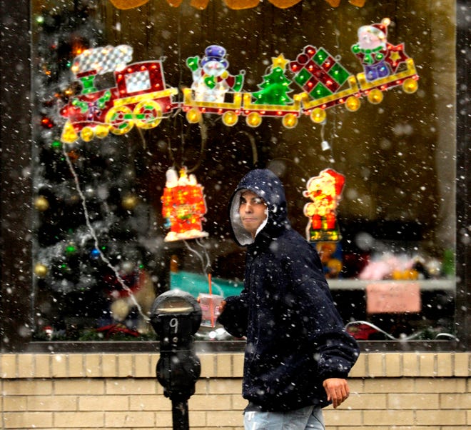 Rafael Costa walks on South Main Street past The Hair Salon's festive windows during Tuesday morning's snowfall.