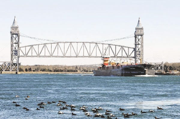 A tug and barge make their way past the railroad bridge as a flock of eider ducks attempt to stay warm.