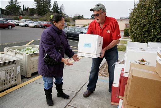This photo taken Jan. 8, 2014 shows Steve Bosshard, right, handing over a specially prepared box of food to Maria Gonzalez, left, at a food bank distribution in Petaluma, Calif., as part of a research project with Feeding America to try to improve the health of diabetics in food-insecure families. Doctors are warning that the federal government could be socked with a bigger health bill if Congress cuts food stamps _ maybe not immediately, they say, but if the poor wind up in doctors' offices or hospitals as a result.