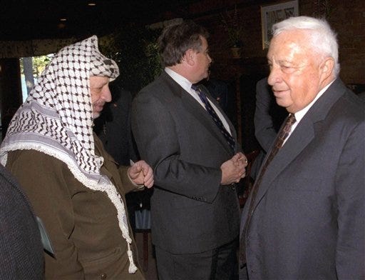 In this Oct. 21, 1998 file photo, Israeli Foreign Minister Ariel Sharon, right, stands near but does not look at, or shake hands with, Palestinian leader Yasser Arafat at Wye Plantation, Maryland. Before becoming a candidate, Sharon proudly boasted he had never shaken hands with Arafat, and called the Palestinian leader a "murderer and a liar" in an interview with the New Yorker magazine. Sharon, the hard-charging Israeli general and prime minister who was admired and hated for his battlefield exploits and ambitions to reshape the Middle East, died Saturday, Jan. 11, 2014. The 85-year-old Sharon had been in a coma since a debilitating stroke eight years ago. (AP Photo/Israel Government Press Office, File)