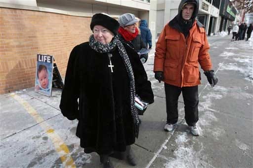 This photo taken Dec. 17, 2013 shows anti-abortion protester Eleanor McCullen, of Boston, left, standing at the painted edge of a buffer zone outside a Planned Parenthood location in Boston. With her pleasant demeanor and grandmotherly mien, McCullen has become the new face of a decades-old fight between abortion opponents asserting their right to try to change the minds of women seeking abortions and abortion providers claiming that patients should be able to enter their facilities without being impeded or harassed. William Cotter of Operation Rescue looks on at right.