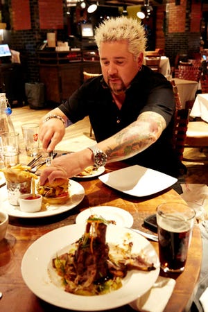 Food Network star Guy Fieri slices into a mac and cheese hamburger as a plate of General Tso's pork shank, foreground, is displayed at his restaurant, Guy's American Kitchen and Bar, on a tour of premier places to get Super Bowl grub in New York.