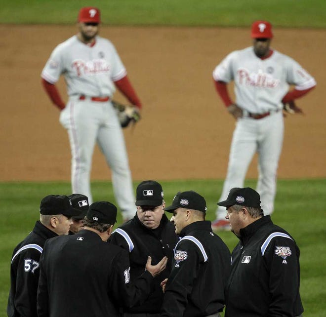 FILE - In this Oct. 28, 2009, file photo, Philadelphia Phillies' Pedro Feliz, left, and Jimmy Rollins watch in the background, as umpires discuss a call at first base during the fifth inning in Game 1 of the baseball's World Series against the New York Yankees in New York. Major League Baseball announced Thursday, Jan. 16, 2014, that it will greatly expand instant replay to review close calls starting this season. Each manager will be allowed to challenge at least one call per game. If he's right, he gets another challenge. After the seventh inning, a crew chief can request a review on his own. (AP Photo/Julie Jacobson, File)