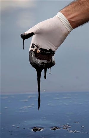 FILE - In this June 15, 2010 file photo, a member of Louisiana Gov. Bobby Jindal's staff wearing a glove reaches into thick oil on the surface of the northern regions of Barataria Bay in Plaquemines Parish, La. Over BP's objections, a federal appeals court on Friday Jan. 10, 2014, upheld a judge's approval of the company's multibillion-dollar settlement with lawyers for businesses and residents who claim the massive 2010 oil spill in the Gulf of Mexico cost them money. (AP Photo/Gerald Herbert, File)