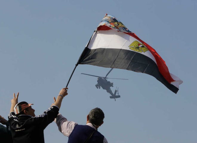 Egyptians wave a national flag as they greet an army helicopter flying over Tahrir Square, the epicenter of the 2011 uprising, in Cairo, Egypt, Saturday.