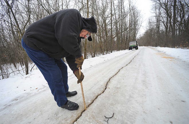 FILE - In this Jan. 11, 2014 photo Dennis Olsen measures a fissure which he said was about an inch wide and at least eight to ten inches deep, in his rural driveway following a frost quake in Waupun, Wis. Known technically as cryoseism, frost quakes are a rare natural phenomena that happen when the temperature drops suddenly, causing moisture in the ground to freeze and expand. They can cause an earthquake-like rumble sometimes with loud, booming noises. (AP Photo/The Reporter, Aileen Andrews, File)