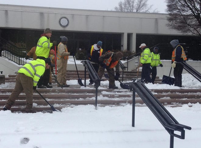 City workers clean snow off the sidewalk in front of Burlington's downtown municipal building.