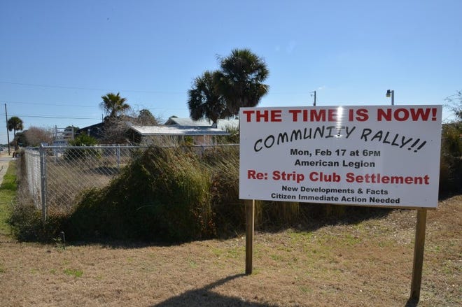 With the site of the proposed strip club in the background, a sign rallies residents to attend a communitywide meeting.